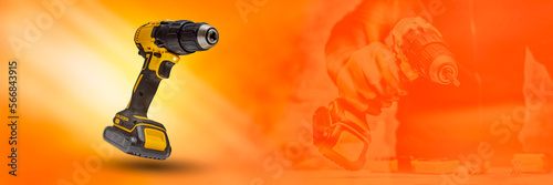 Man worker holds an electric screwdriver in his hands close-up against the background of a construction tool on a orange background. Long banner with glow effects. photo