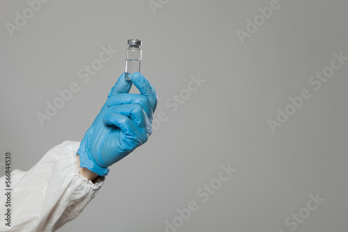 Closeup of vial to vaccinate in scientific virologist hand for immunization. Scientific virologist. Biologist in protective suit and blue gloves. Vaccination concept.