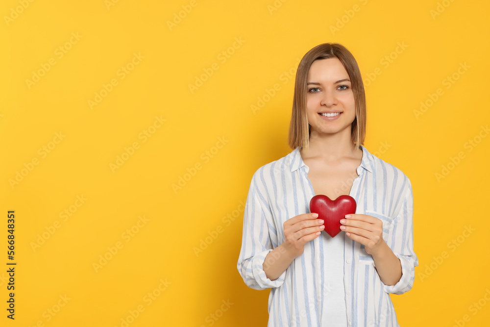 Young woman holding red heart on yellow background, space for text. Volunteer concept Young woman holding red heart on yellow background, space for text. Volunteer concept