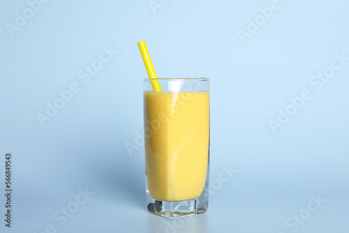 Glass of tasty smoothie with straw on light blue background