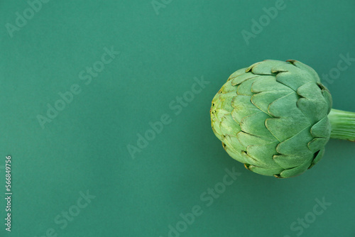 Whole fresh raw artichoke on green background, top view. Space for text