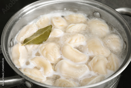 Cooking dumplings (varenyky) with tasty filling and bay leaf in pot, closeup