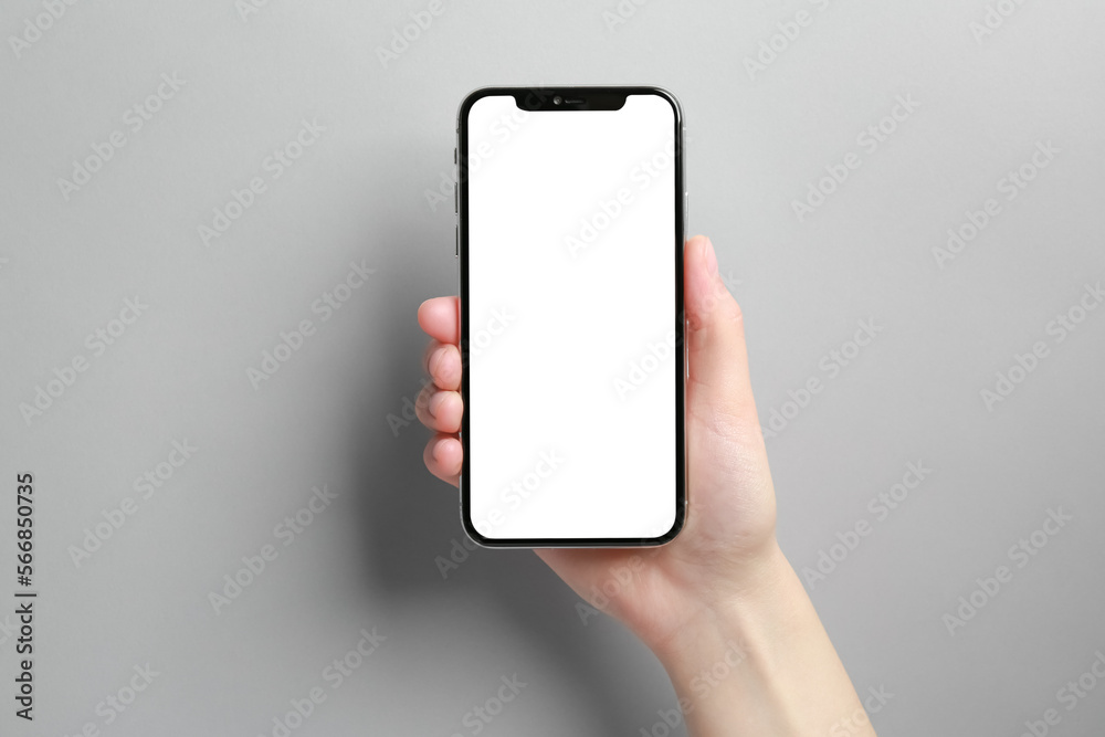 Woman holding smartphone with blank screen on grey background, closeup. Mockup for design Woman holding smartphone with blank screen on grey background, closeup. Mockup for design