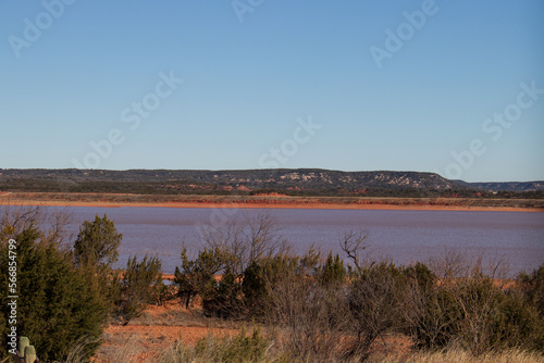 Fototapeta Naklejka Na Ścianę i Meble -  A view of Lake Abilene with the red clay shoreline and the rolling hills of Texas in the background at Abilene State Park, Texas