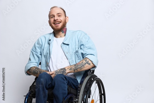 A man in a wheelchair smile, copy space, with tattoos on his arms sits on a gray studio background, the concept of health is a person with disabilities, a real person