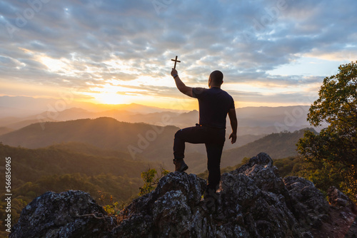 Male Travel holding christian cross praying alone on top mountain sunset background Lifestyle spiritual relaxation emotional concept vacations outdoor harmony with nature landscape