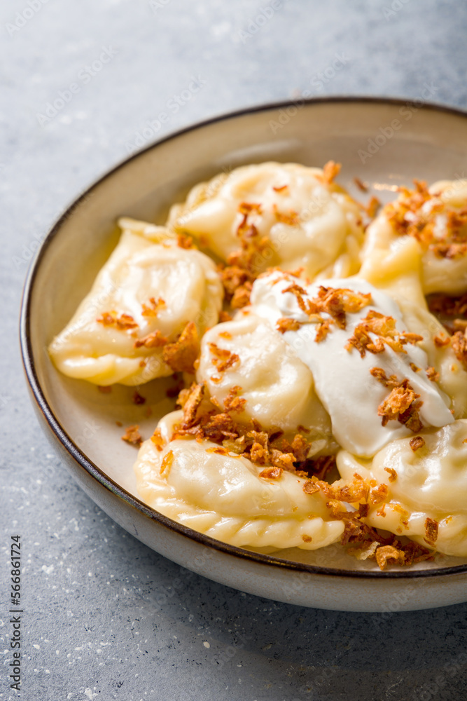 dumplings with potatoes and fried onion with sour cream on a plate vertical macro close up