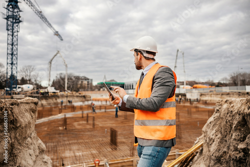 Фотография A builder is standing on construction site and checking on works on tablet