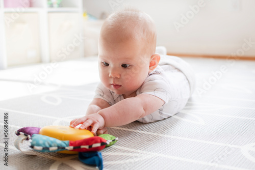 Little baby girl is playing with a toy during tummy time. Baby reaching for a musical toy. Baby development