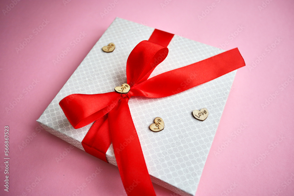 Paper gift box decorated with red ribbon by a woman's hand, gift wrapping for a gift on a special day, top view.