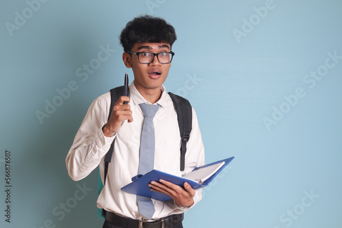 Indonesian senior high school student wearing white shirt uniform with gray tie holding some books, smiling and looking at camera. Isolated image on blue background photo