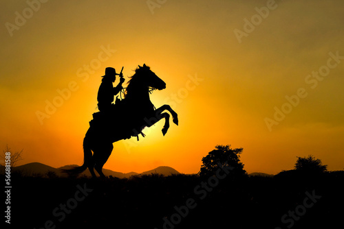 An original 1800s western cowboy rides his forefoot in the sunset across the prairie with the mountains in the background.
