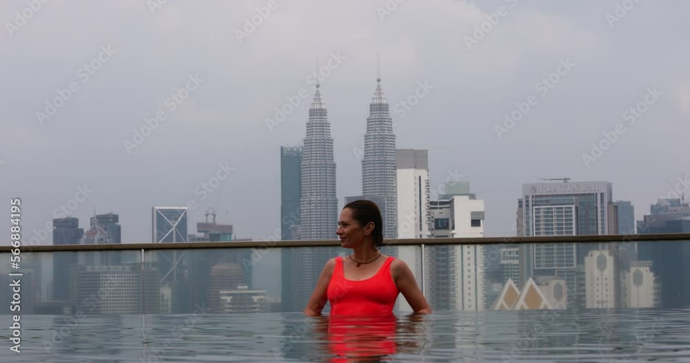 A woman stands with her back against the glass side of outdoor pool ...
