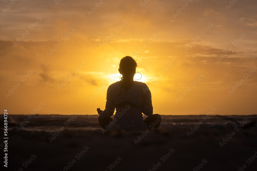 Woman practicing yoga on the beach against the light during sunrise