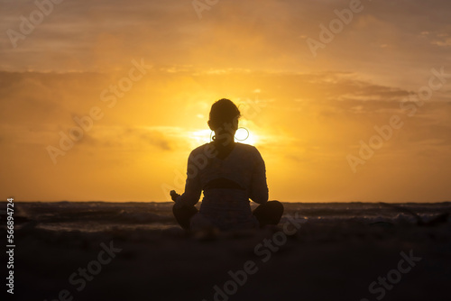 Woman practicing yoga on the beach against the light during sunrise