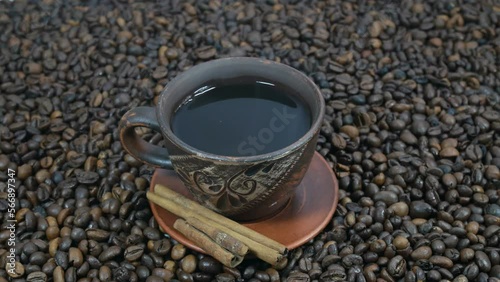 A cup of hot coffee stands on the table next to coffee beans. Cinnamon sticks for coffee are very tasty. Coffee beans background for advertising. photo