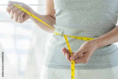 Young slim woman measuring her waist by measure tape after a diet