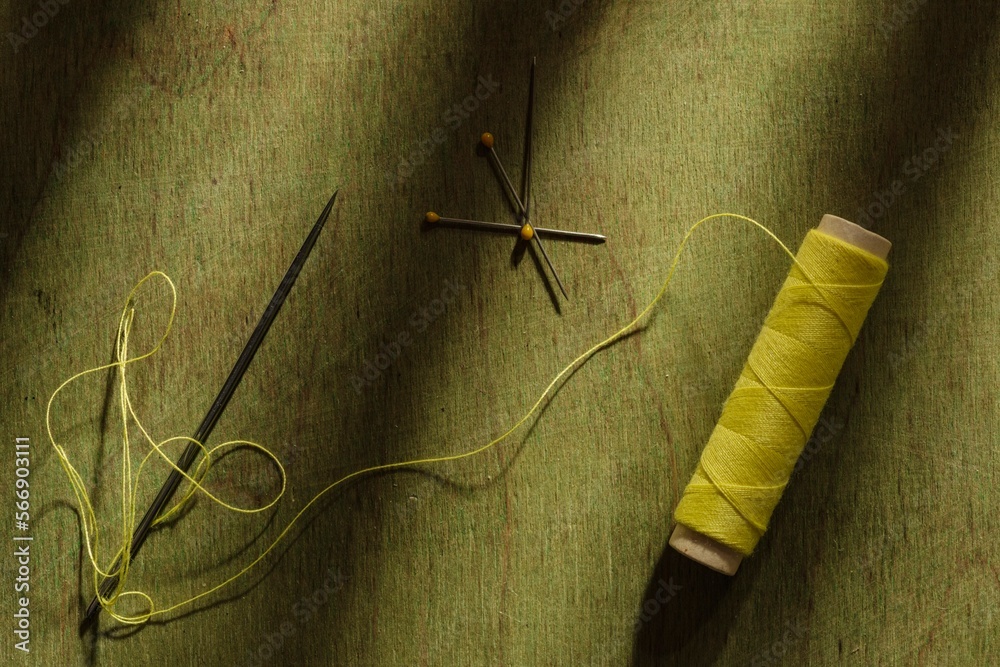 Spool of yellow thread and needles on a dark wooden background