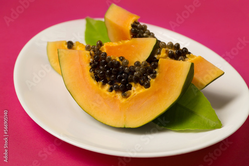 papaya cut into pieces in a plate on a pink Viva Magenta color background