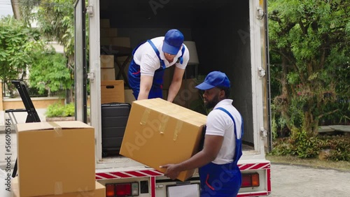 Workers unloading boxes from van outdoors.House move, mover service and Moving service concept.Two young handsome smiling workers wearing uniforms are unloading the van full of boxes.