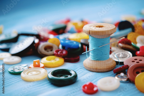 A bunch of colored buttons and a spool of thread and a needle. Tailor