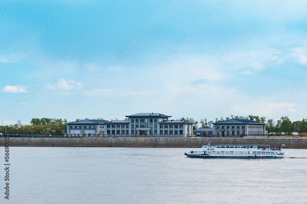 A Russian pleasure boat floats along the river against the backdrop of the Chinese embankment with buildings and a blue sky with clouds. Summer sunny day.