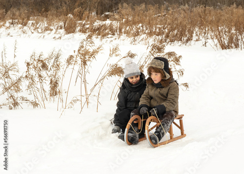 Two boys of 8 years old are walking in the forest. Friends cheerfully walk across a snow-covered field. Winter forest in the background. High quality photo