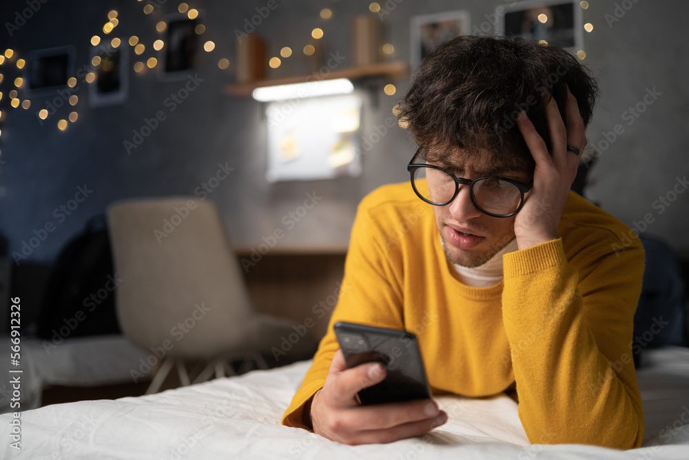 Man is upset while using smartphone in the evening lying on bed. Man is upset while using smartphone in the evening lying on bed.