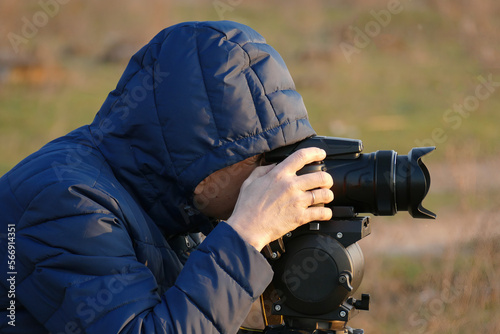 Photographer man in a hood shoots a super zoom photo.