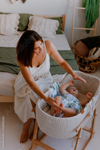Little baby lying in crib and young mother sits about it. happy family.