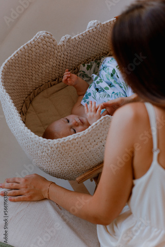 Little baby lying in crib and young mother sits about it. happy family.