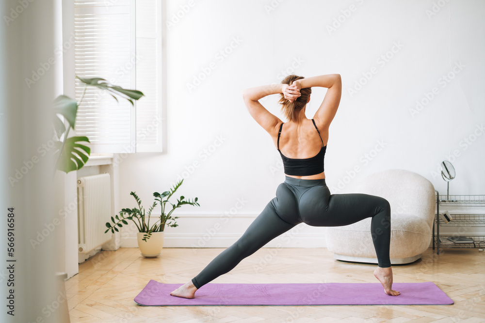 Young slim woman in sportwear doing fitness exercises in living room at home