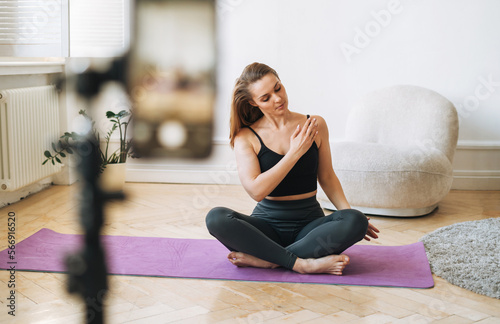 Young woman fitness blogger doing exercises and recording video on mobile phone phone in studio