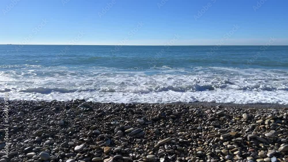 Powerful sea waves are crashing on the Black Sea coast. Sea waves splash on the beach with pebbles in the rays of the sun. Russia, Agoi