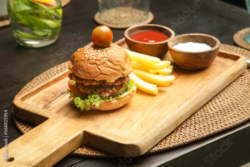 Small size burger served with french fries and sauces on the wooden board in cafe