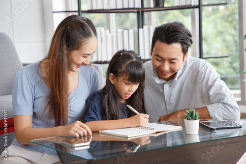 Children education and home school concept   Young asian father and mother see little daughters  study. Excited smiling small child girl enjoying learning and writing with pleasant dad and mom at home