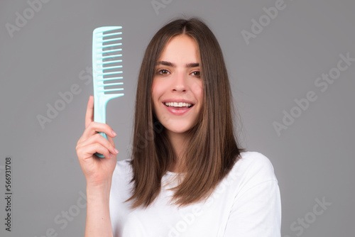Portrait of beautiful young woman combing her hair, smiling. Female brushing healthy hair with comb. Cares about a healthy and clean hair. Beauty salon concept.