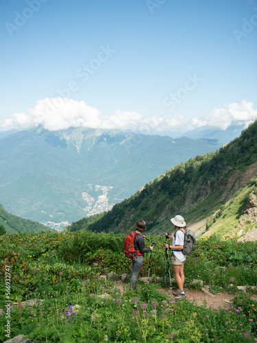  Two women with backpacks and trekking poles hiking in mountains enjoying the view during sunny day