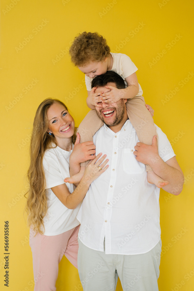 Happy parents hugging their son, expressing love, warm feelings. The child is sitting on the father's neck. Having fun family isolated yellow background. Happy parents hugging their son, expressing love, warm feelings. The child is sitting on the father's neck. Having fun family isolated yellow background.
