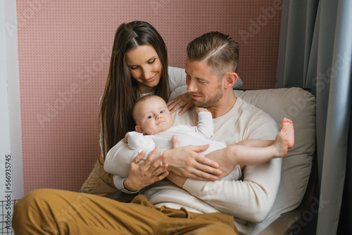 Young happy parents hold their baby son in their arms and smile looking at him
