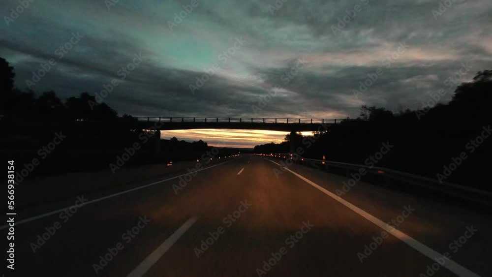 Driving on empty long asphalt road in the night with dusk sunset in background over a cloudy sky. Travel truck car expedition destination. Transport with vehicle on the road. Bridge on freeway