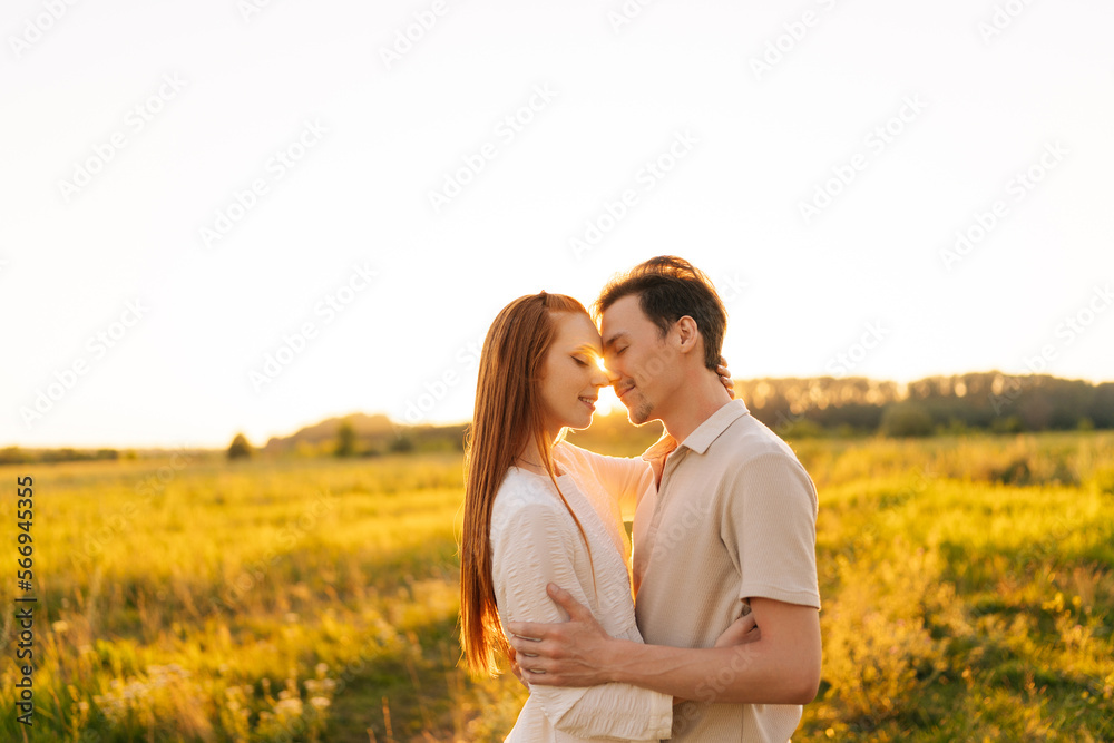 Portrait of loving young couple in relationship hugging and kissing enjoying each other in wonderful sunlight of sunset on green meadow. Romantic man and woman spending unforgettable moments together. Portrait of loving young couple in relationship hugging and kissing enjoying each other in wonderful sunlight of sunset on green meadow. Romantic man and woman spending unforgettable moments together.