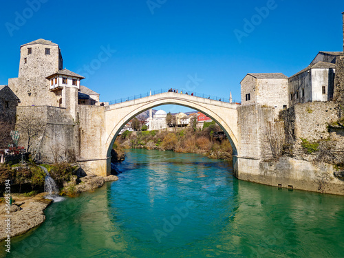 Aerial drone view of the Old Bridge in Mostar city in Bosnia and Herzegovina during sunny day. Blue turquoise colors of Neretva river. Unesco World Heritage Site. People walking over the bridge.
