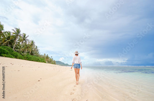 Vacation on the seashore. Back view of young woman walking away on the beautiful tropical white sand beach. © luengo_ua