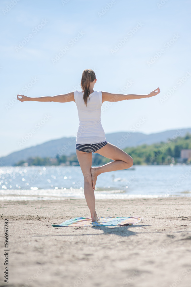 Frau am Strand mit glitzernden Wasser in der Yoga Baum Pose im Sommerurlaub in Italien Frau am Strand mit glitzernden Wasser in der Yoga Baum Pose im Sommerurlaub in Italien