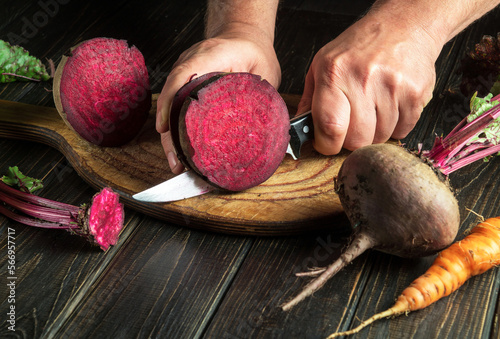 Wall Mural Hands of a cook with a knife cut beetroot to prepare delicious borscht