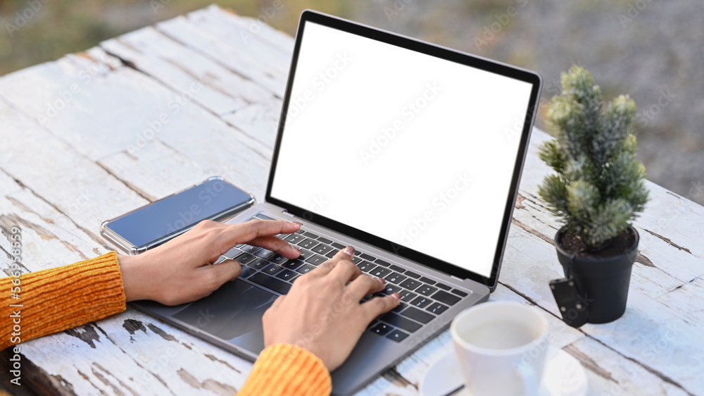 Fototapeta premium Close up view of young female freelancer hands typing on laptop computer while sitting at outdoor cafe
