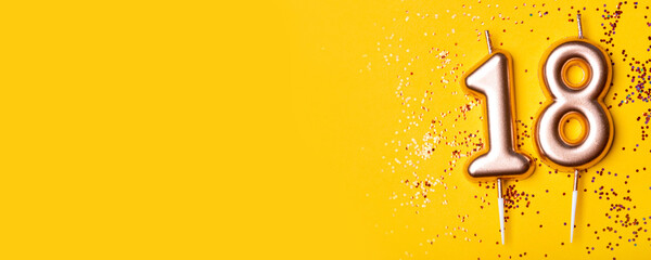 Gold candles in the form of number eighteen on yellow background with confetti. 18 years celebration. Greeting banner.