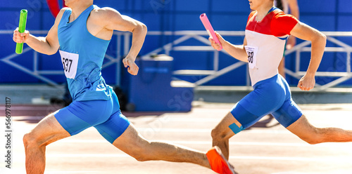two male athletes with relay baton in hands run at competition