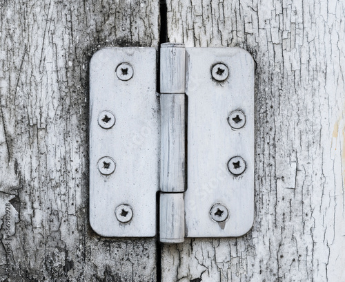 Old and worn big heavy white painted metal hinge against a worn wooden door.